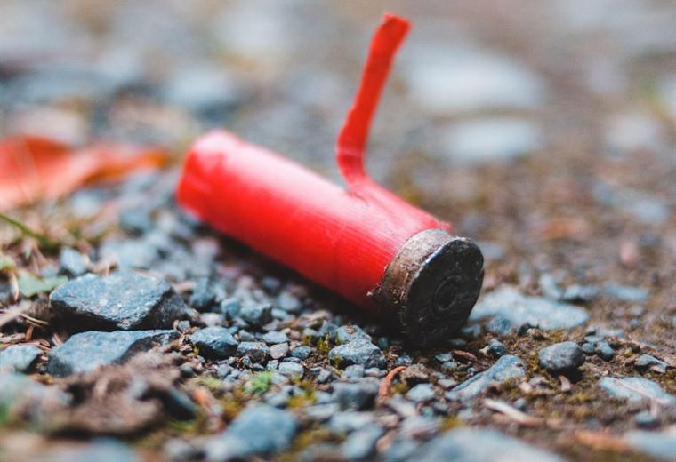 A red shotgun shell resting on wet stones