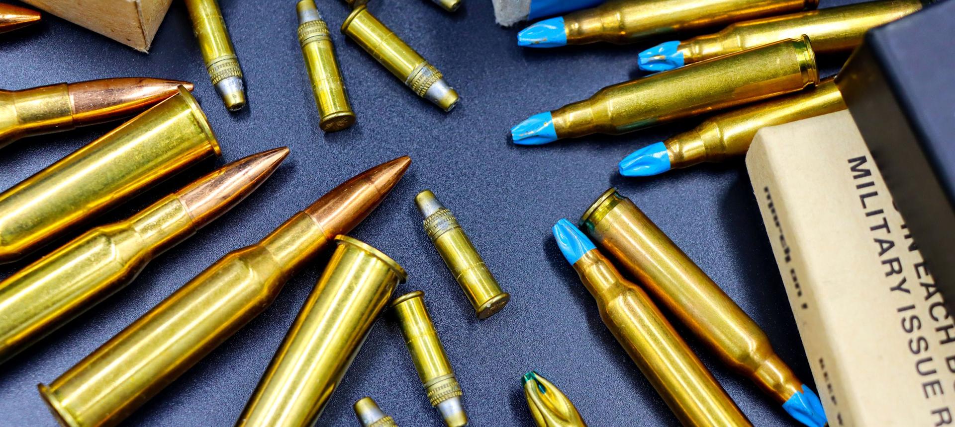 Brass rifle and pistol cartridges laid out beside their boxes on a dark surface
