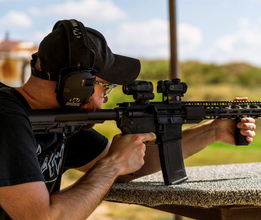 A shooter in ear and eye protection firing a rifle at an outdoor range